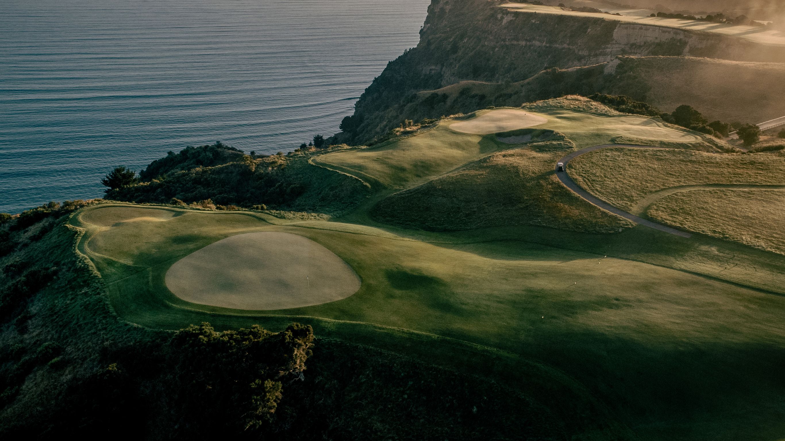 A coastal golf course atop rugged cliffs, with rolling fairways, greens, and stunning views of steep hills and the ocean.